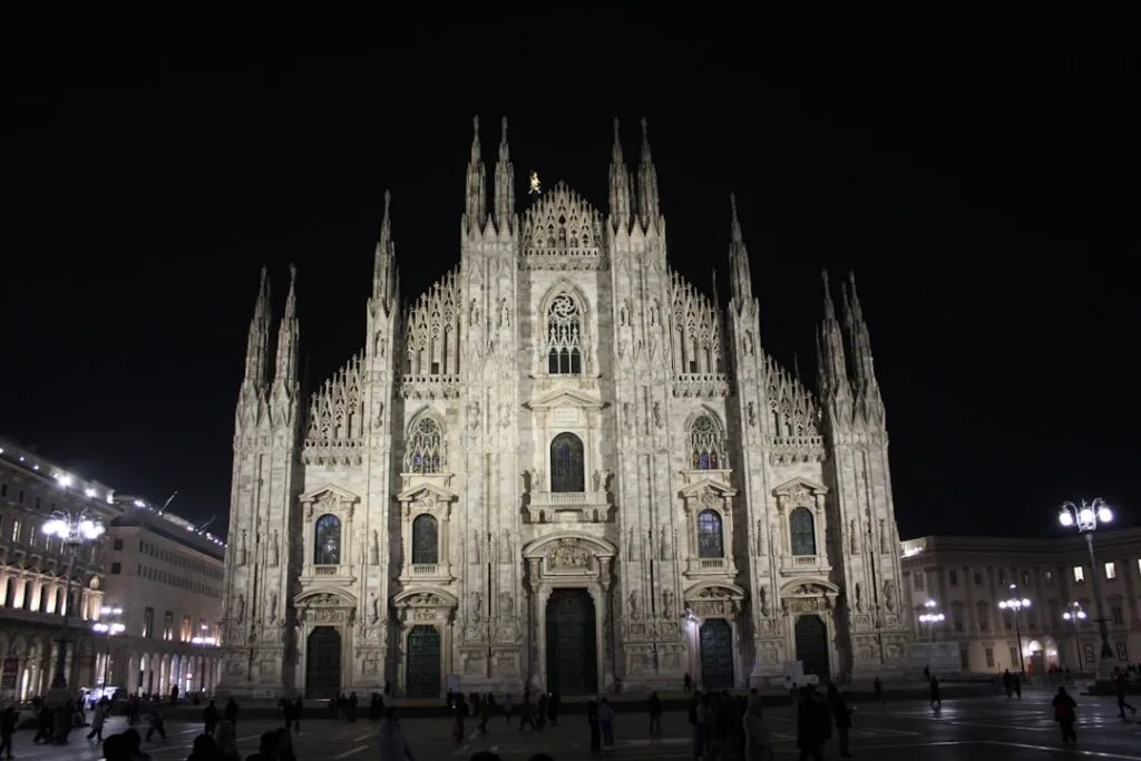Façade éclairée du Duomo de Milan la nuit, place animée