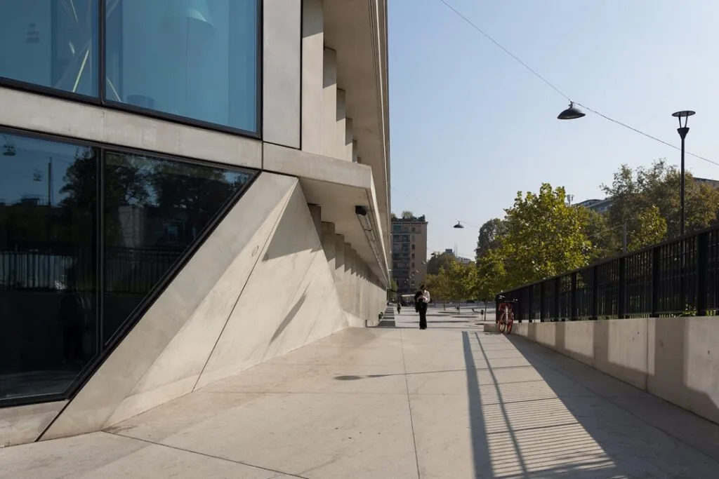 Passage piéton devant bâtiment en béton angulaire, personne et vélo, Milan