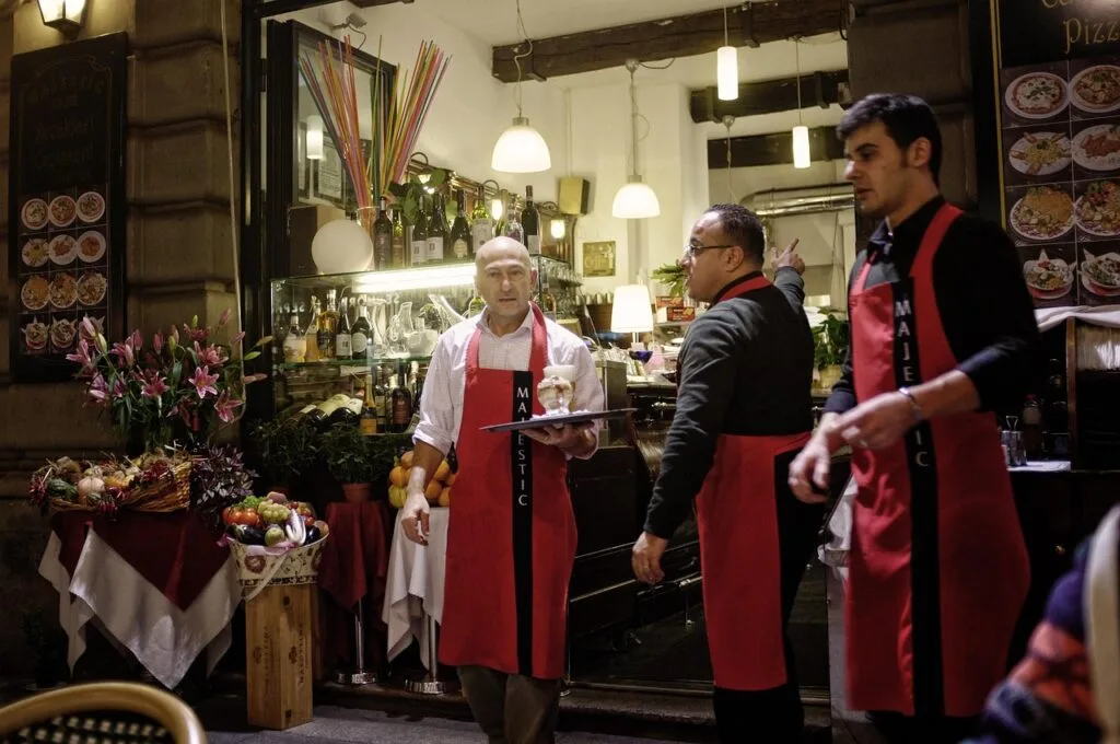 Serveurs en tabliers rouges devant un restaurant animé de Milan
