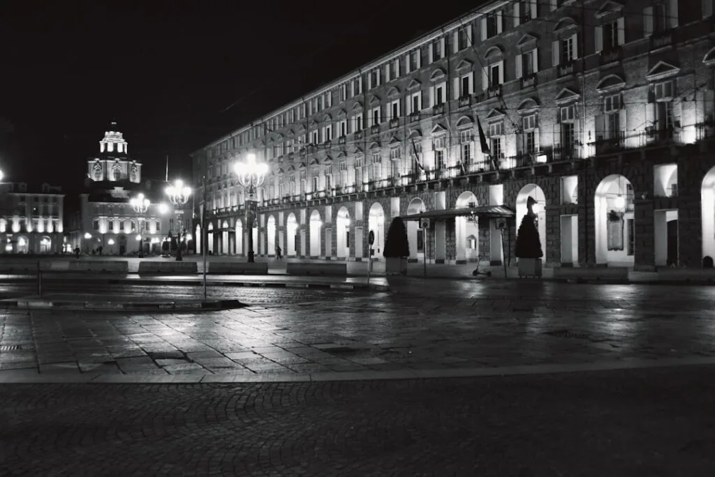 Place pavée nocturne aux arcades éclairées et lampadaires.