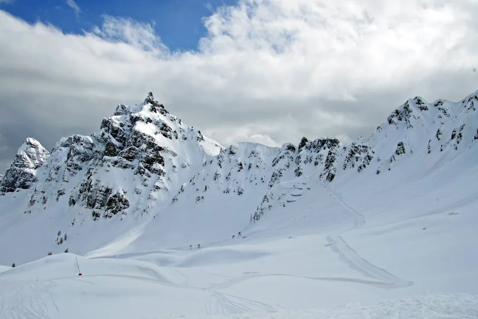 Paysage de montagnes enneigées avec traces de ski sous un ciel nuageux