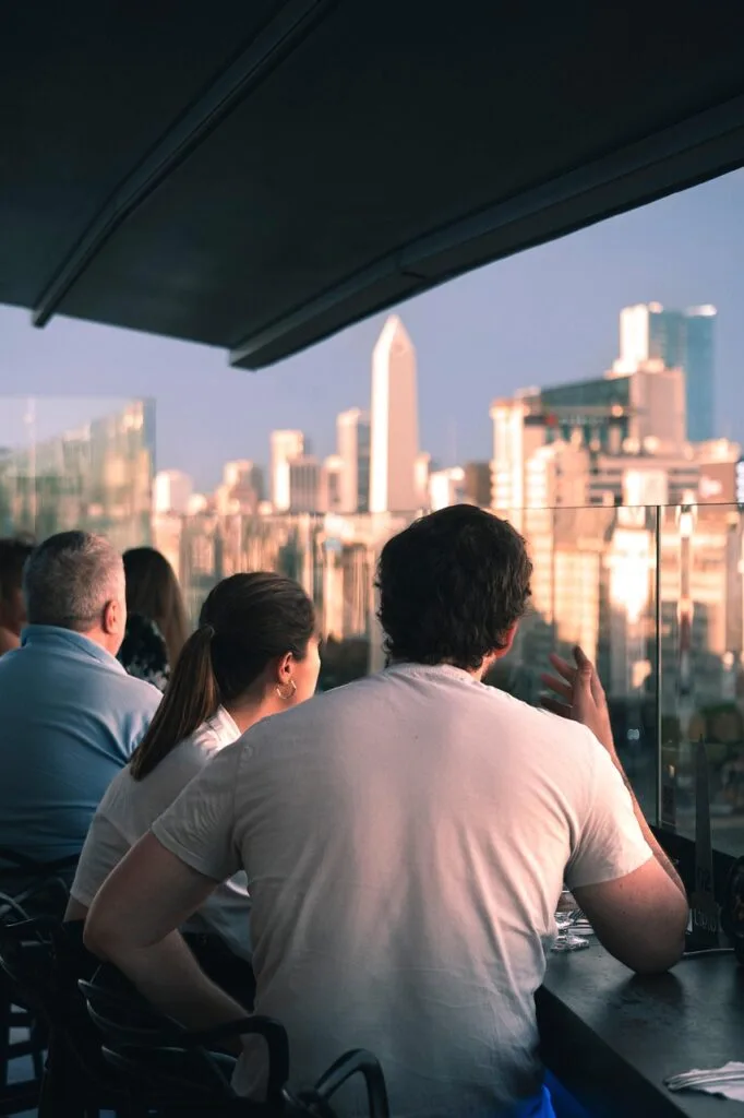 Groupe attablé sur terrasse avec vue urbaine au coucher du soleil