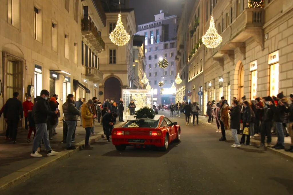 Voiture de sport rouge entourée de passants et décorations de Noël à Milan