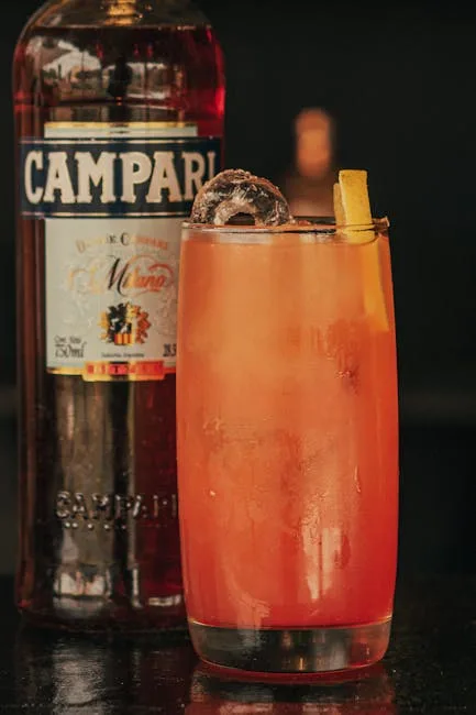 Long drink orangé glacé décoré d'un zeste devant une bouteille Campari