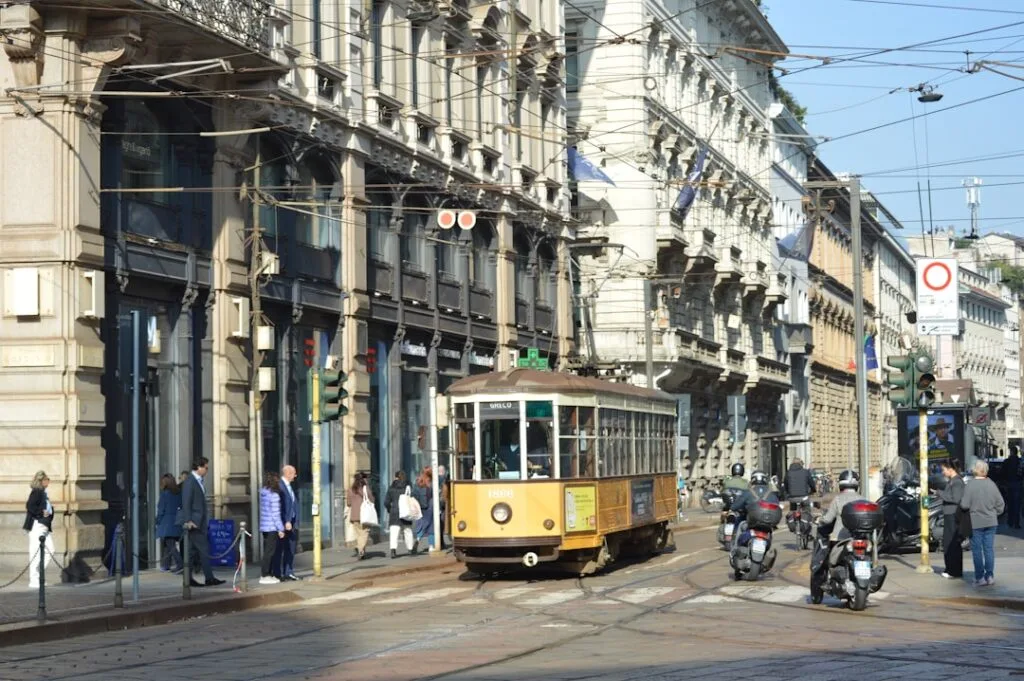Oud gele tram rijdt door drukke winkelstraat met scooters in Milaan